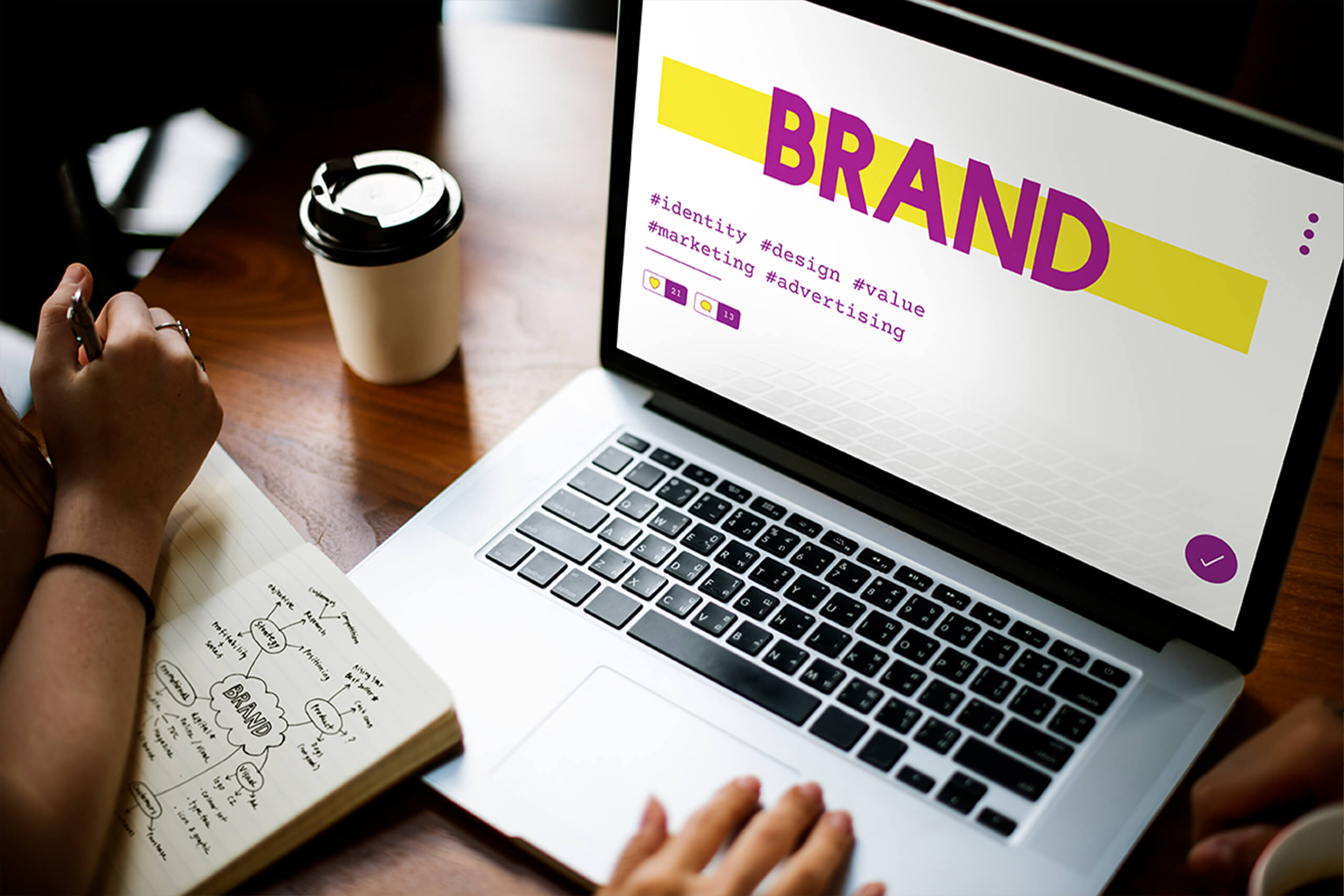 DotClick: A laptop displaying "BRAND" on its screen with branding materials and a coffee cup, representing brand identity creation.